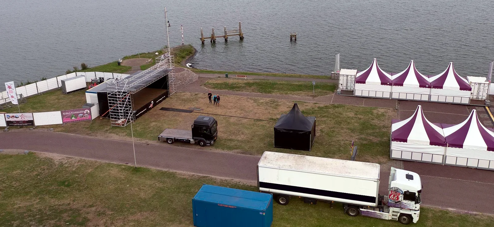 Een evenemententerrein aan het water met pagodetenten en vrachtwagens