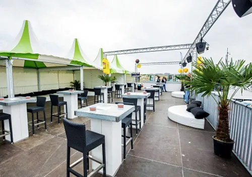 Een loungeterras met statafels, krukken en groene parasols