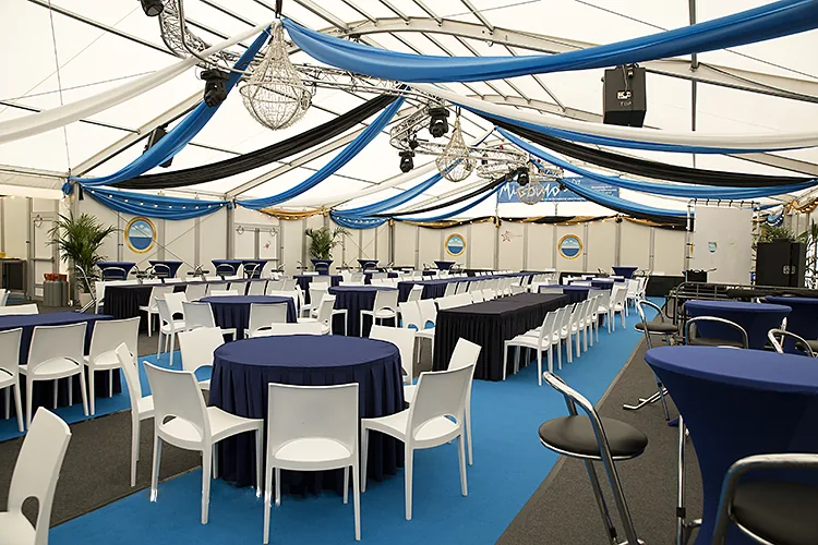 Tent van binnen met blauwe hemelbekleding, ronde tafels en witte stoelen