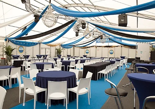 Ronde tafels met blauwe kleden en witte stoelen in een tent