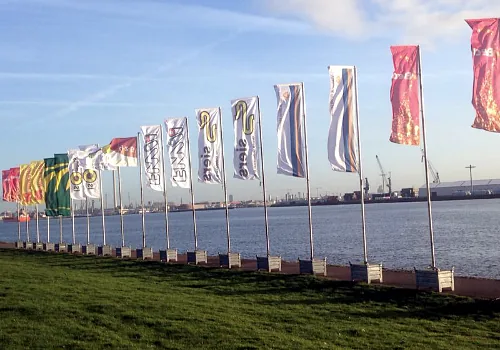 Een rij vlaggenmasten met wapperende vlaggen langs het water